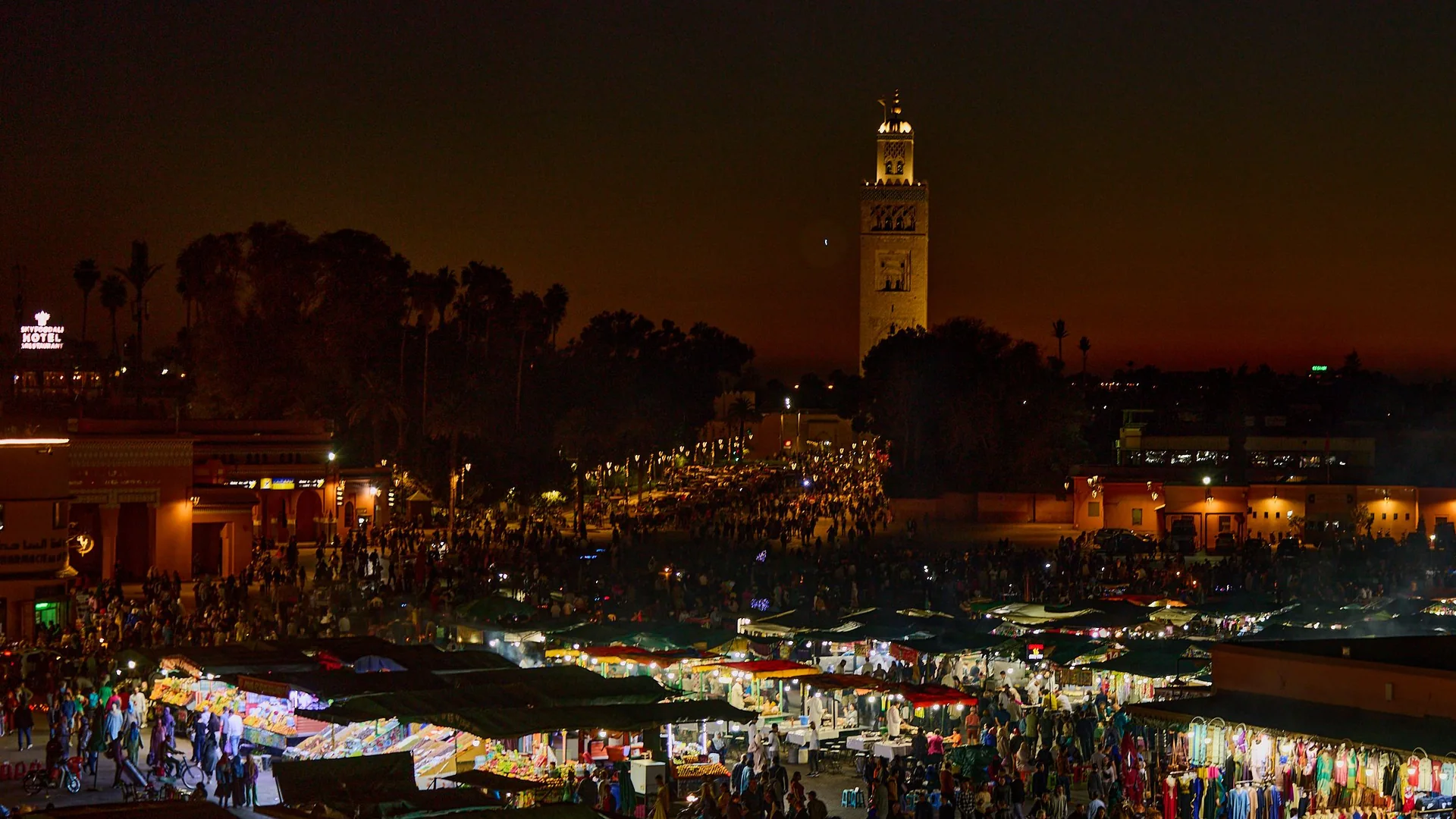 The lit Koutoubia minaret rises above the stalls and crowds of Jemaa el-Fnaa in Marrakech just after sunset