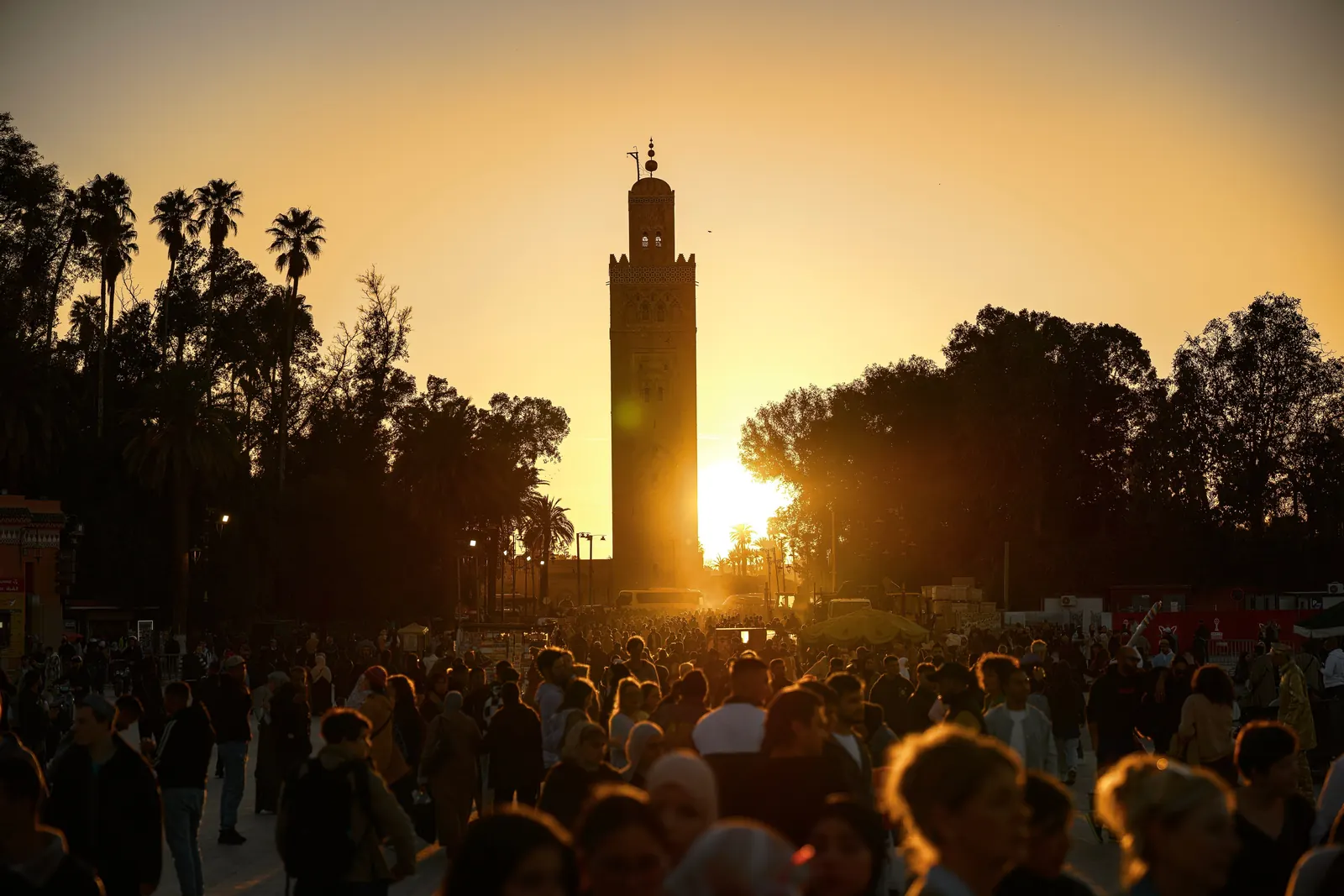 The Koutoubia minaret stands against a gold sunset above a crowd in Marrakech