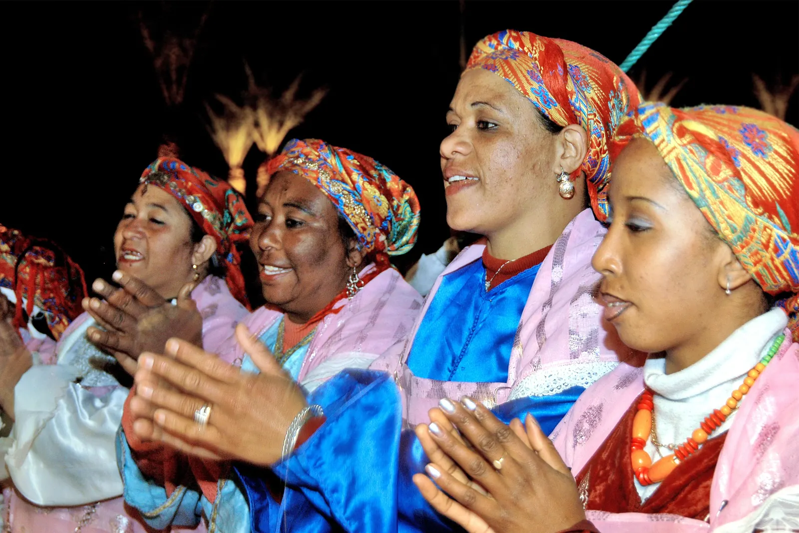 Women in bright headscarves and silk jackets clap and sing at a Moroccan evening celebration
